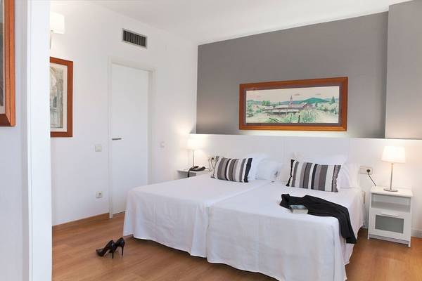 Zweibettzimmer im Atenea Barcelona Aparthotel mit zwei weißen Betten, Kissen und Decken, Nachttischen und Lampen.