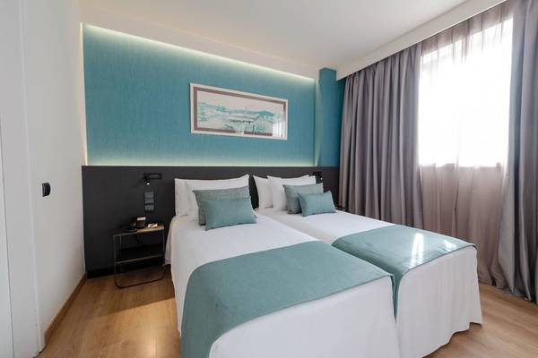 Zwei Doppelbetten in einem stilvollen Zimmer im Atenea Barcelona Aparthotel mit blauer Wand und einem Bildrahmen.