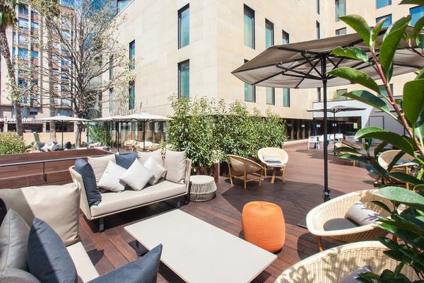 Terrasse im Ocean Drive Barcelona Hotel mit Loungemöbeln und einem großen Sonnenschirm.