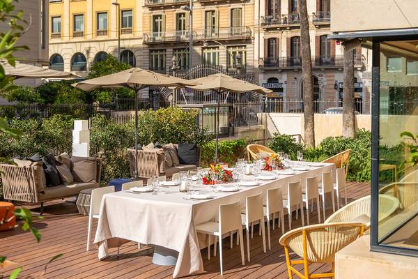 Terrasse im Ocean Drive Barcelona mit langem Tisch, Blumen, Stühlen und Sonnenschirmen