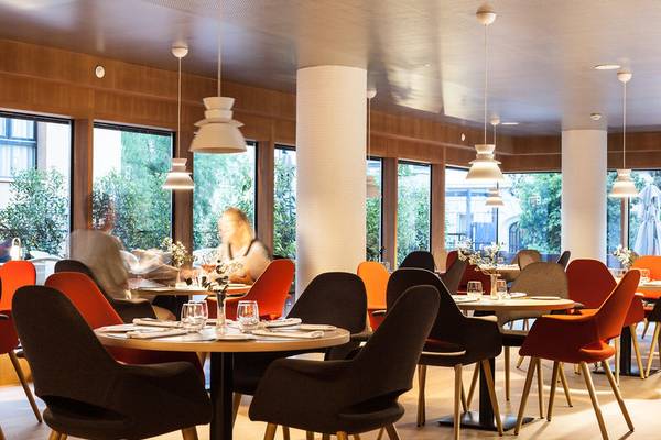 Innenansicht des Ocean Drive Barcelona Restaurants mit runden Tischen, orangefarbenen Stühlen und großen Fenstern.