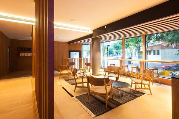 Innenbereich des Ocean Drive Barcelona Hotels mit Holzmöbeln, Tischen und Stühlen vor großen Fenstern.