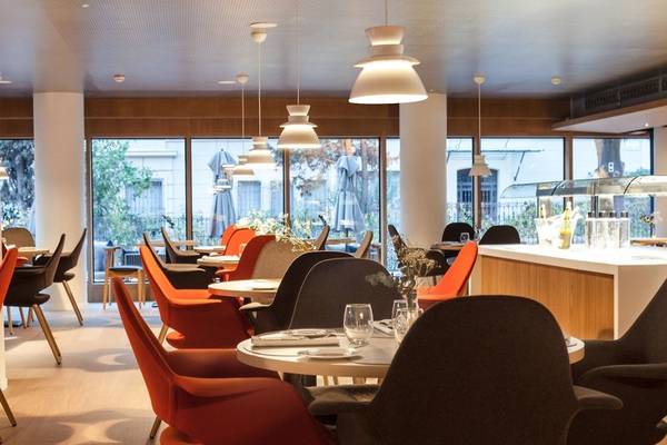 Innenraum des Ocean Drive Barcelona Restaurants mit runden Tischen und Stühlen, großen Fenstern und Deckenlampen.