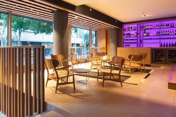 Innenraum des Ocean Drive Barcelona Hotels mit Holzmöbeln, großen Fenstern und einer gut bestückten Bar.