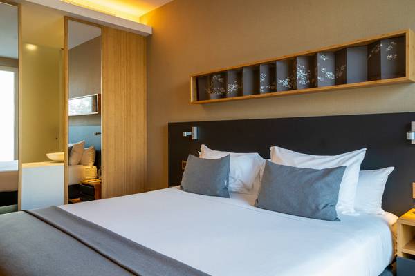 Hotelzimmer im Ocean Drive Barcelona mit einem großen Bett, grauen Kissen und einem beleuchteten Wandregal.