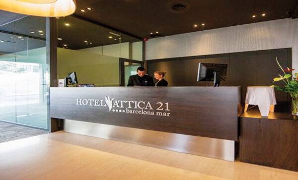 Rezeptionsbereich des Hotels Attica 21 Barcelona Mar mit zwei Mitarbeitern und einem großen Logo.