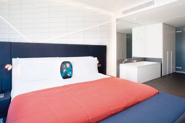 Innenansicht des Schlafzimmers im W Barcelona Hotel mit einem großen Bett, Nachttisch und Lampe.