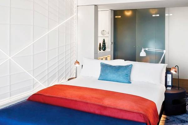 Schlafzimmer im W Barcelona Hotel mit weißem Bett, blauem Kissen und leuchtenden Textilien.