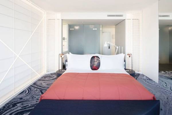 Innenansicht des Schlafzimmers im W Barcelona Hotel mit einem Bett, weißen Kissen und roter Decke.