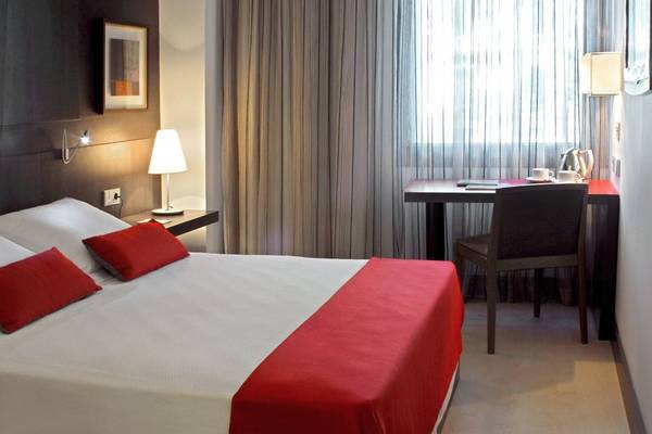 Doppelbettzimmer im Grupotel Gran Via 678 Hotel mit rotem Laken und Kopfkissen, Schreibtisch und Stuhl.