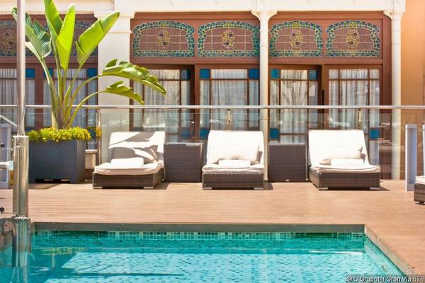 Pool-Lounge-Sessel vor dem Grupotel Gran Via 678 mit blauen Fenstern und Pflanzen.