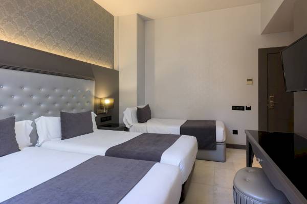 Hotelzimmer im Ciutadella Barcelona mit drei Betten, modernem Design und weißem Interieur.
