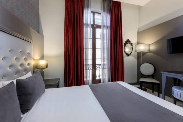Schlafzimmer im Ciutadella Barcelona Hotel mit einem Bett, Kissen, Nachttischen und einem Fenster.