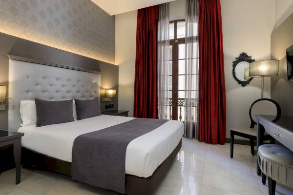 Innenansicht eines modernen Hotelzimmers im Ciutadella Barcelona, mit Bett, Nachttischen und einem Balkon.
