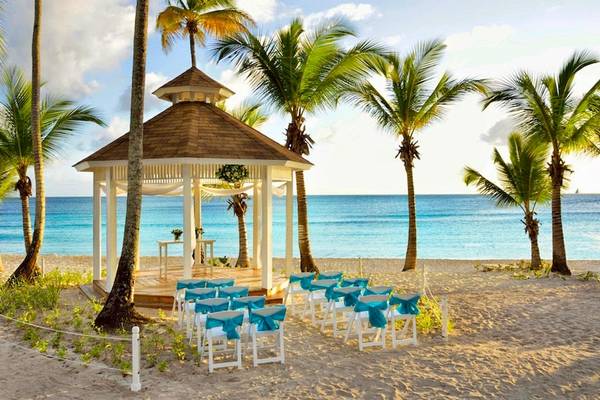 Hochzeitszelt am Strand des Catalonia Bayahibe Hotels mit blauen Stühlen und Palmen.