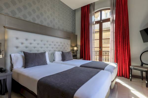 Doppelbett-Zimmer im Ciutadella Barcelona Hotel mit rotem Vorhang und Fenstern.