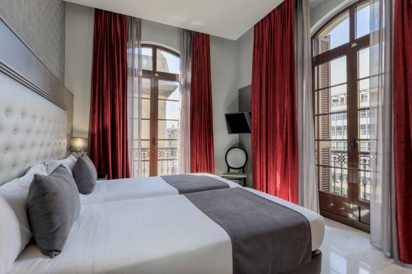Doppelbett-Zimmer im Ciutadella Barcelona Hotel mit zwei Betten, roten Vorhängen und Balkon.