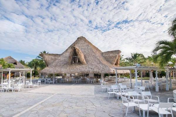 Außenbereich des Catalonia Bayahibe Hotels mit terrassendach und weißen stühlen und tischen.