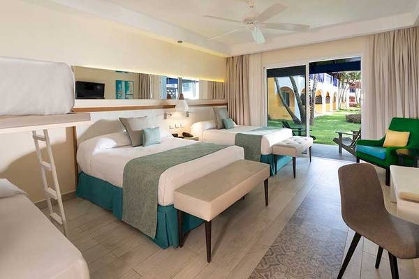 Hotelzimmer im Catalonia Bayahibe mit drei Betten, Schreibtisch und Balkonzugang.