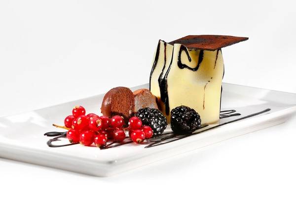 Dessert auf weißem Teller mit roten und schwarzen Beeren und Schokoladenstückchen.