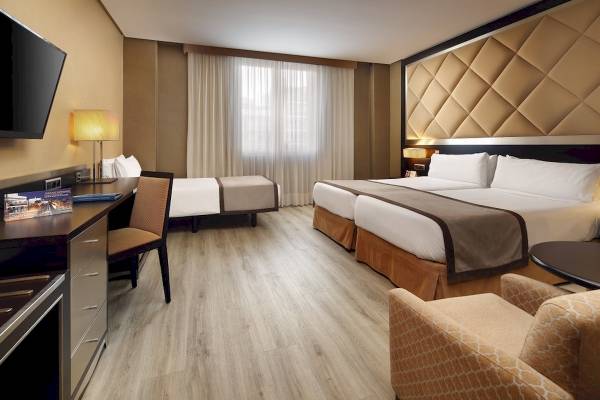 Hotelzimmer im HCC St. Moritz mit zwei Betten, Schreibtisch, Stühlen und Fernseher.