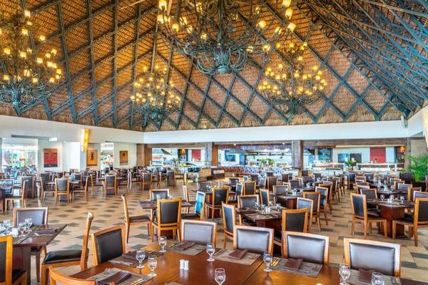 Innenansicht des Restaurants im Hilton La Romana mit vielen Tischen und Stühlen, großen Kronleuchtern und einer offenen Dachkonstruktion.