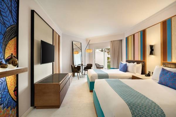 Innenansicht eines Doppelzimmers im Hilton La Romana mit zwei Betten, Fernseher, Tisch und Stühlen.