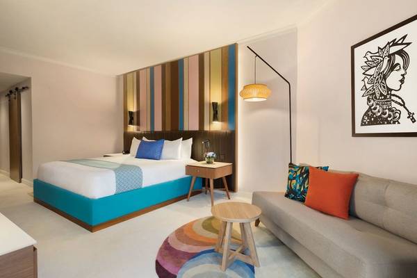 Innenansicht eines Hotelzimmers im Hilton La Romana mit Bett, Couch, Tisch und Wanddekoration.