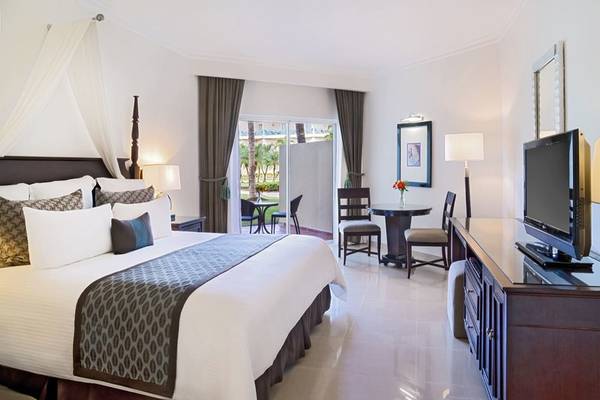 Ein elegantes Schlafzimmer im Hilton La Romana mit einem großen Bett, Fenstern und einer Aussicht auf Palmen.