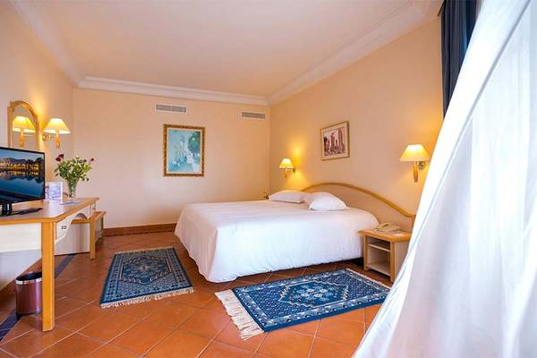 Hotelzimmer im Medina Belisaire & Thalasso mit Bett, Fernseher, Tisch und orientalischen Teppichen.