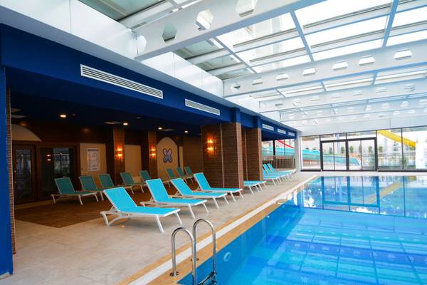 Innenpoolbereich des Diamond Premium Hotel & Spa mit blauen Liegen und Glaswänden.