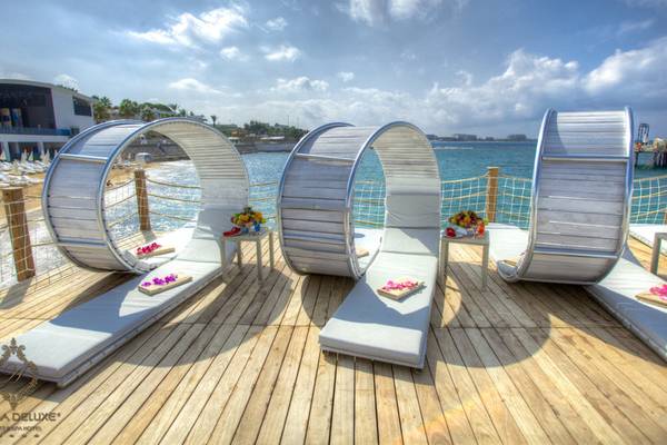 Vier weiße runde Liegestühle auf der Terrasse des Azura Deluxe Resort & Spa mit Blick auf das Meer.