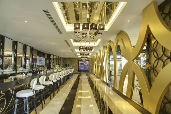 Innenansicht der Bar im Azura Deluxe Resort & Spa mit goldenen Wänden und weißen Stühlen.