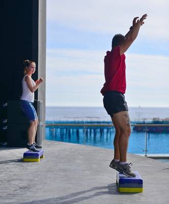 Zwei Personen stehen auf Steigen mit Blick auf das Meer und eine Pier im Hintergrund.