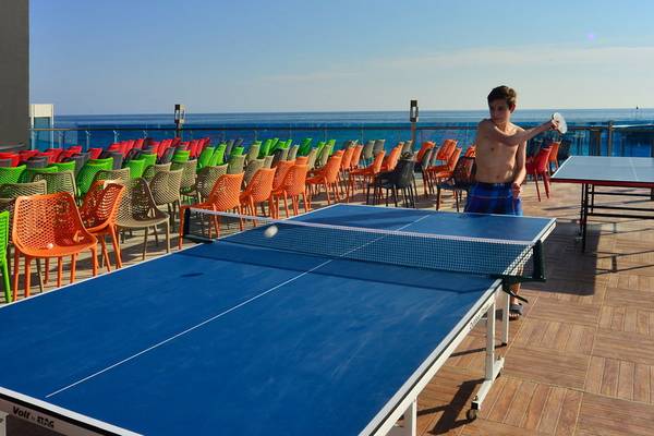 Junger Mann spielt Tischtennis auf der Terrasse des Azura Deluxe Resort & Spa mit Blick auf das Meer.