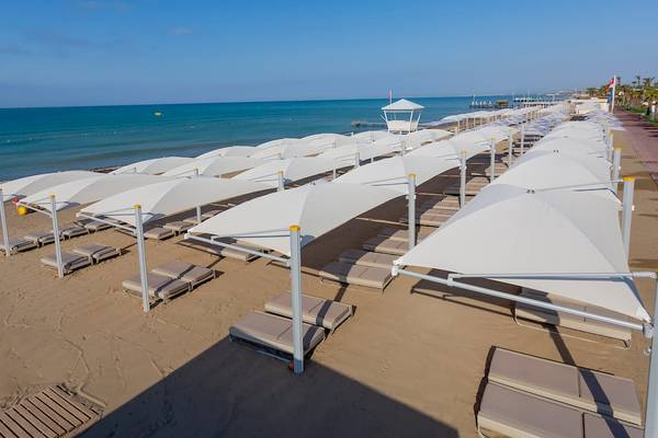 Strand des Hotels Güral Premier Belek mit weißen Sonnenschirmen und Liegen
