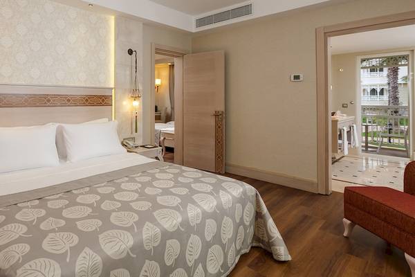 Güral Premier Belek Hotelzimmer mit Bett, Balkontür und Wohnzimmer
