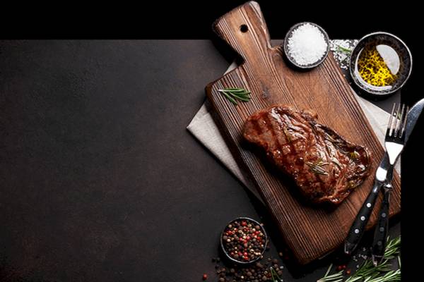Ein gewürztes Steak liegt auf einem Schneidebrett mit Rosmarin und Gewürzen.