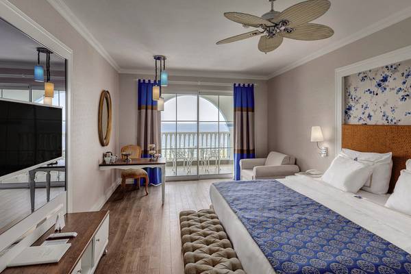 Ein modernes Hotelzimmer mit Blick auf das Meer, einschließlich eines großen Bettes, eines Schreibtisches und einer Terrasse.
