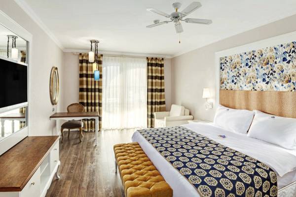 Ein modernes Hotelzimmer mit einem großen Bett, einem Nachttisch, einem Schreibtisch, einem Sessel, einem Spiegel und einer Klimaanlage.