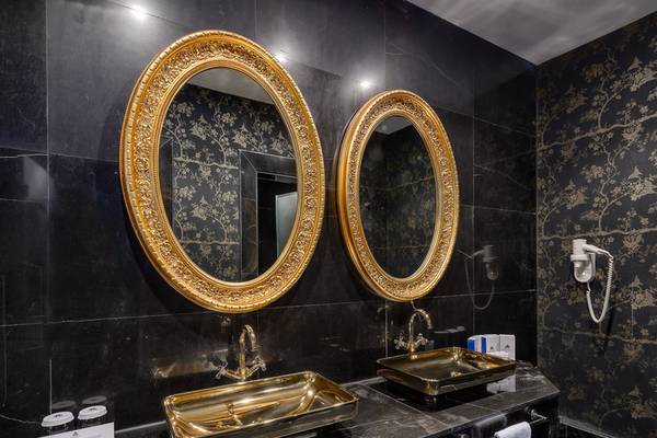 Ein Badezimmer mit zwei goldenen Waschbecken und Spiegeln, schwarzen Marmorwänden und goldenen Mustern.