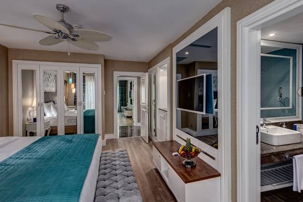 Schlafzimmer und Badezimmer der Rubi Platinum Spa Resort & Suites mit blauem Bett, Fernseher und Badezimmerspiegel.