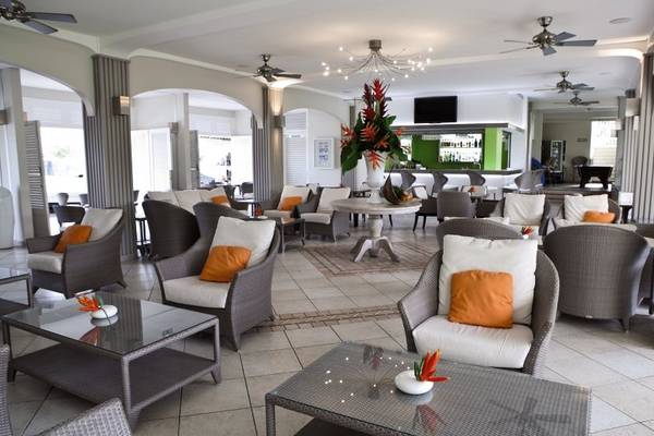 La Pagerie - Tropical Garden Hotel Lounge mit weißen Möbeln und orange Kissen.
