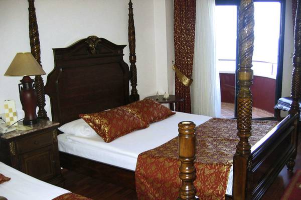 Doppelbett im Delphin Deluxe Hotel mit roten Seidenkissen und Holzbettpfosten.