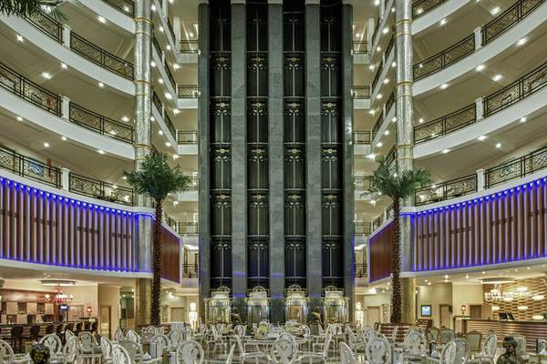 Foyer des Delphin Deluxe Hotels mit vielen Tischen und Stühlen, hohen Säulen und blauen Lichtern.