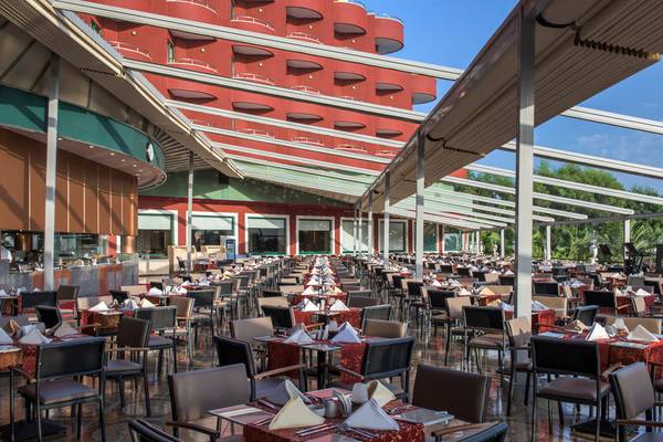 Außenbereich des Delphin Deluxe Hotels mit vielen gedeckten Tischen und Sonnenschutz.