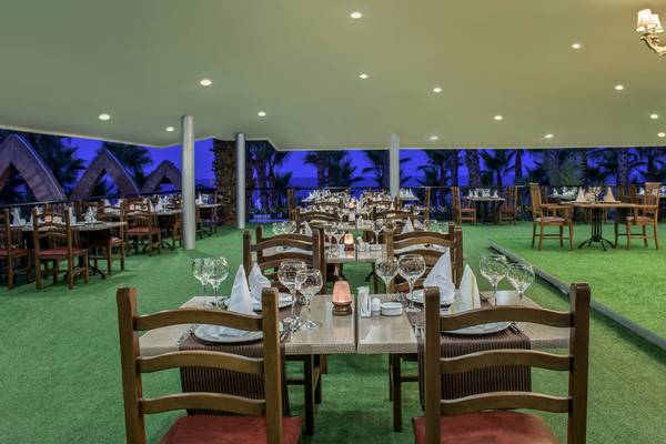 Innenbereich des Delphin Deluxe Hotel Restaurants mit gedeckten Tischen und Stühlen auf grünem Teppich.