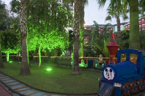 Ein Micky Maus Zug im Delphin Deluxe Hotel Garten mit grünen Lichtern und Bäumen.