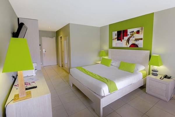 Schlafzimmer im La Pagerie - Tropical Garden Hotel mit grünen Wänden, weißer Bettwäsche und grünen Kissen.