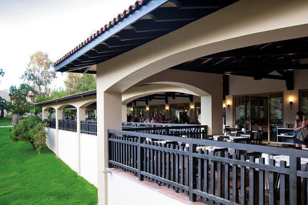 Restaurantbalkon im Melas Holiday Village mit grüner Rasenfläche und bestuhlten Tischen.